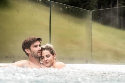 Pärchen im Whirlpool auf der Dachterrasse des Adults Only Wellnessbereichs im Familienhotel Feuerstein in Südtirol