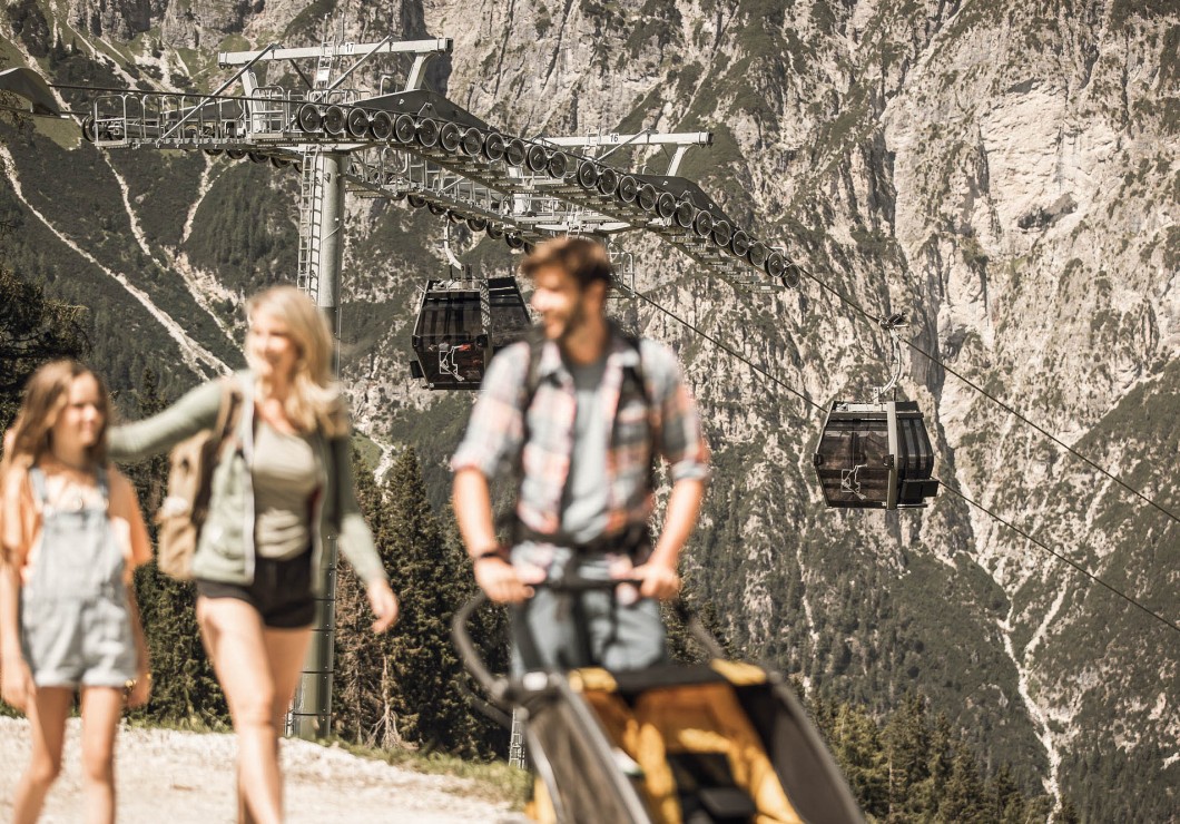 A man, a woman and a child out walking; behind them, you can see the cable cars from Ladurns