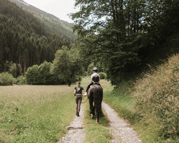 A child is riding with a riding instructor in the woods at a children's hotel in South Tyrol.