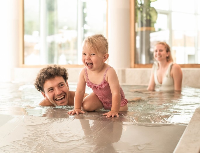 Una bambina sta giocando con la sua famiglia nella piscinetta dell'hotel per famiglie in Alto Adige, dotato di scivolo acquatico