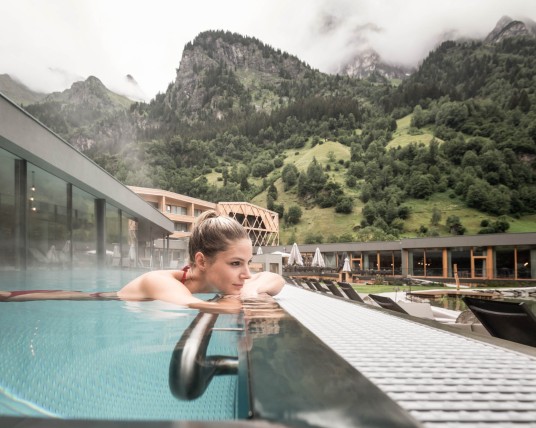 Una donna si sta godendo la piscina a sfioro all'aperto di un hotel per famiglie dotato di scivolo acquatico in Alto Adige.