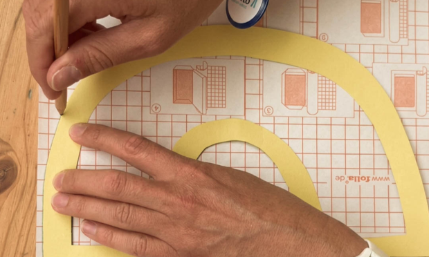 The cut-out rainbow is placed on a self-adhesive sheet and the outer and inner outlines are traced onto it.