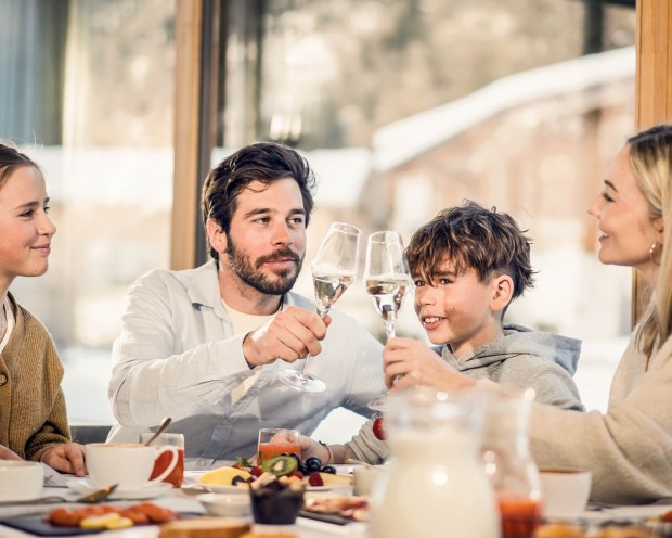 Eine Familie genießt ihr Frühstück und Eltern stoßen mit Prosecco an.