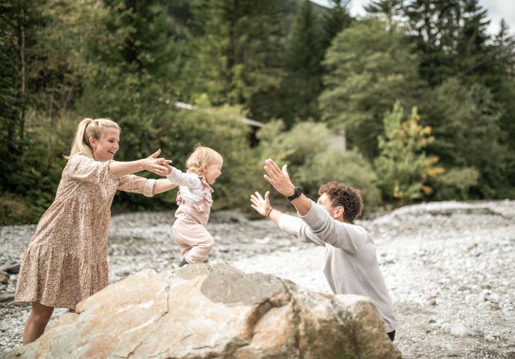 Bambino piccolo in piedi su una grande pietra che apre le braccia per abbracciare papà