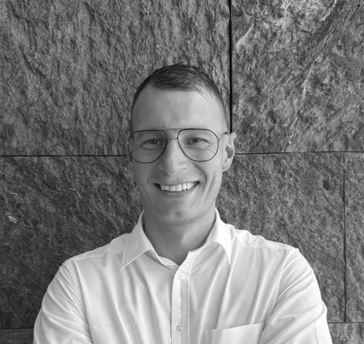 Fabian, our executive assistant, is standing in front of a black wall, smiling at the camera with his arms crossed.