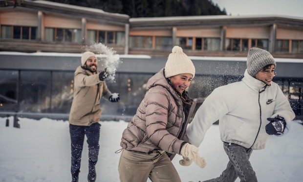Vater bewirft Tochter und Sohn mit einem Schneeball. Alle haben großen Spaß.