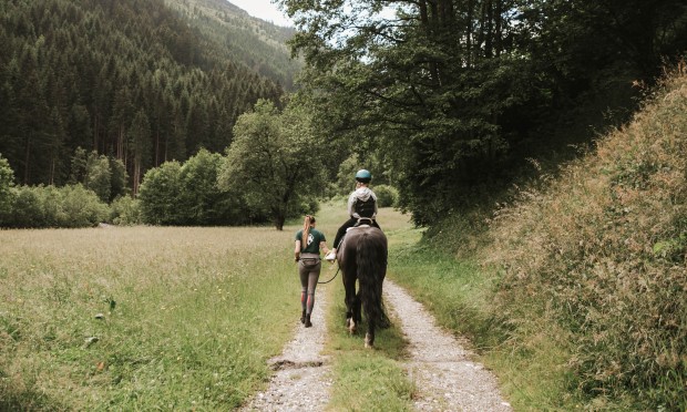 Horse with a child riding and a riding instructor taking a walk through the forest