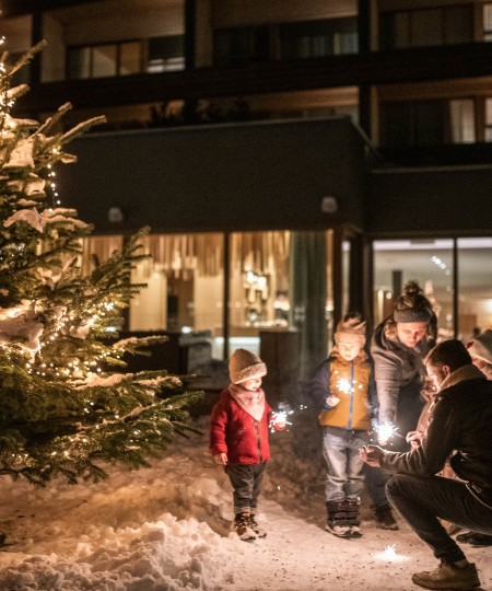Familie steht vor dem Haus und vor dem Christbaum und zünden einen Sternspritzer an.