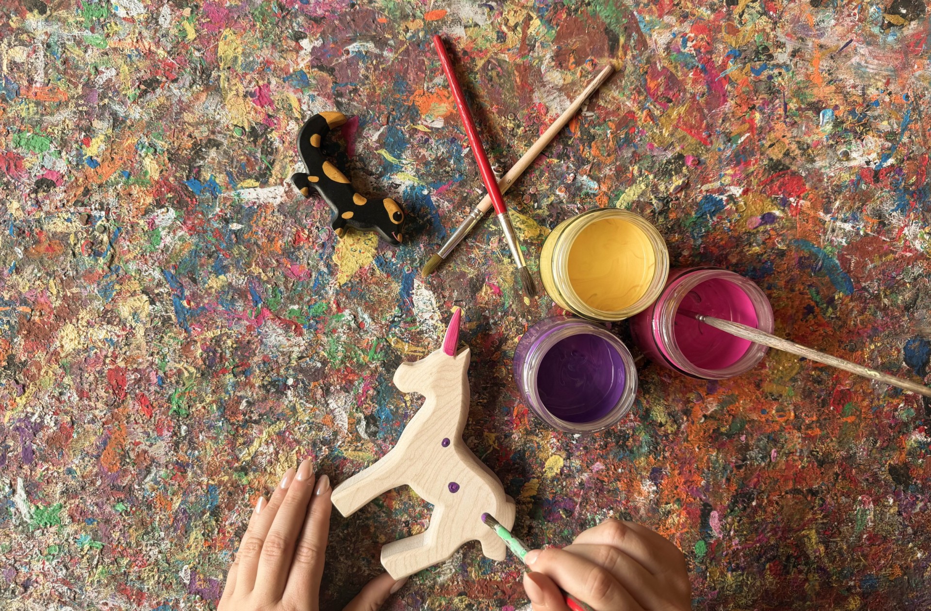 Le mani impugnano i pennelli e dipingono piccoli puntini sull'unicorno di legno