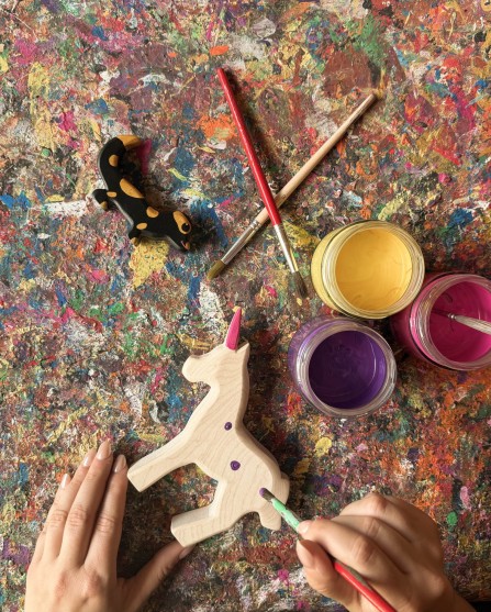 Le mani impugnano i pennelli e dipingono piccoli puntini sull'unicorno di legno