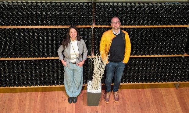 Director Julia Auckenthaler and Deputy Director Massimo stand in front of a large wine rack.