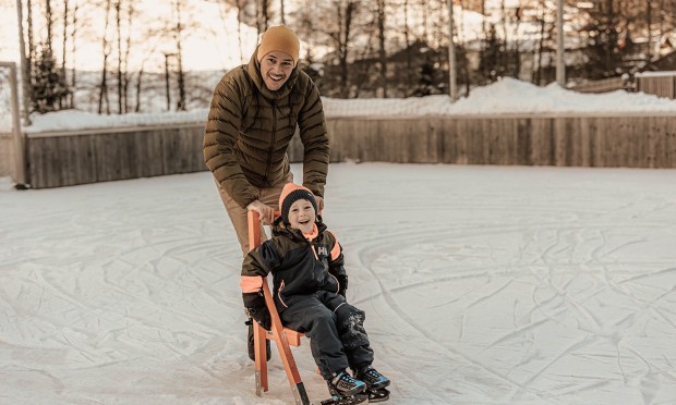 Un padre impara a pattinare con suo figlio e lo spinge lungo il ghiaccio con l’aiuto per l’apprendimento.