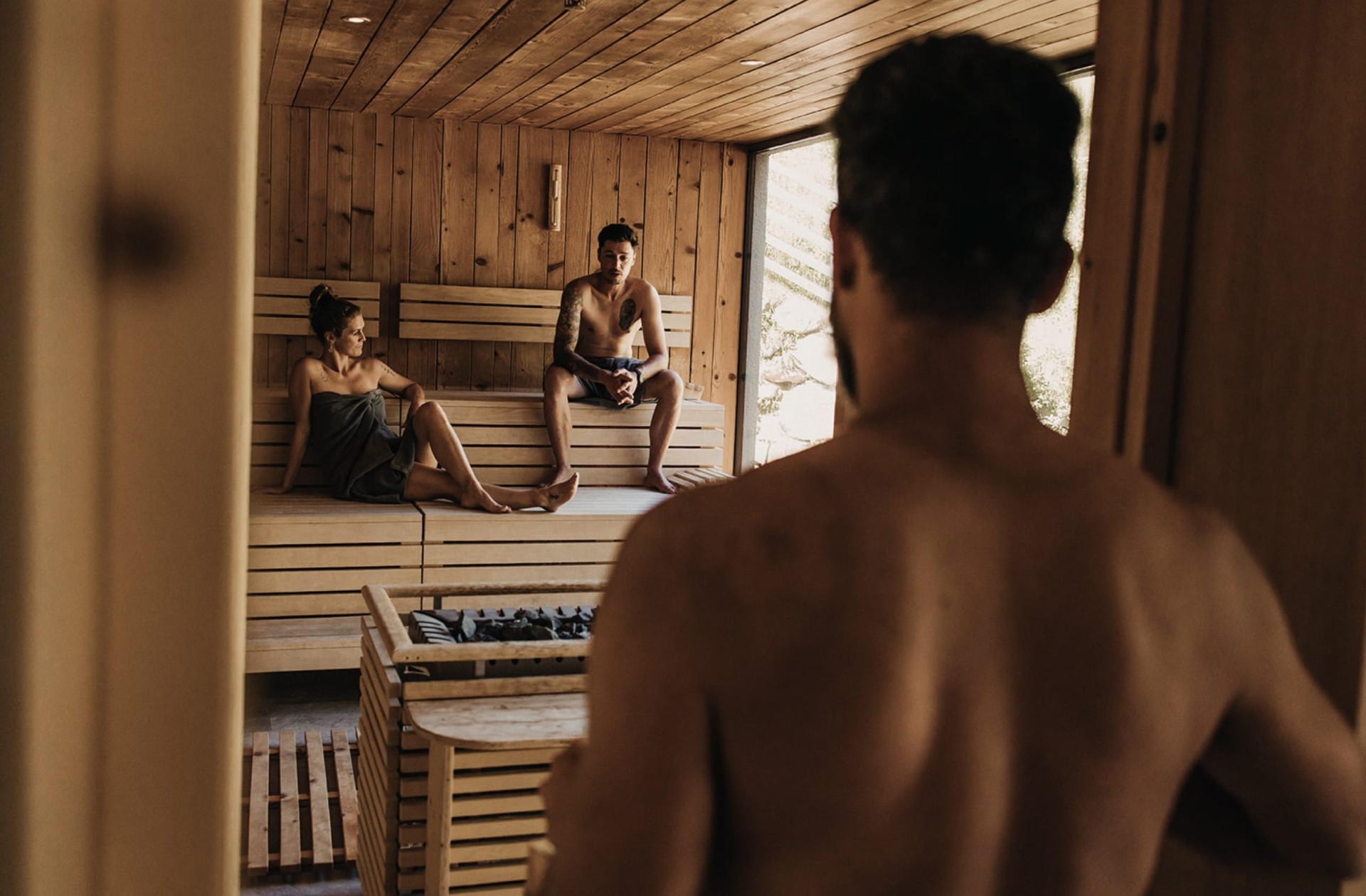 Tre persone sedute in sauna mentre un uomo entra nella cabina.