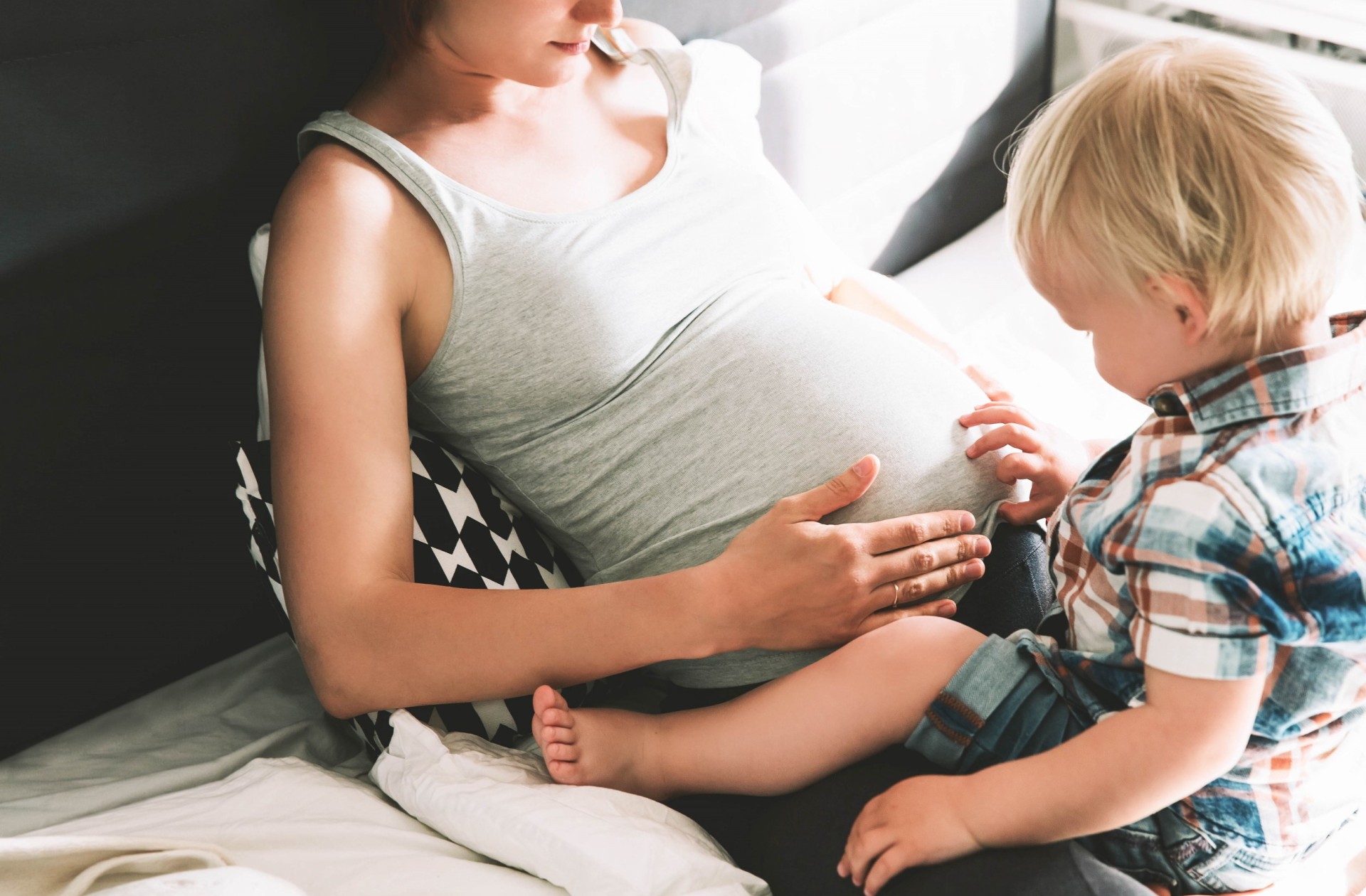 Kleiner Junge begutachtet den schwangeren Bauch seiner Mutter