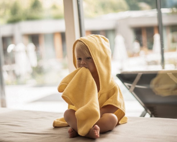 Kleines Kind sitzt mit einem gelben Bademantel