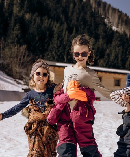 Tre bambini sorridenti in abbigliamento da sci posano sulla neve con occhiali da sole
