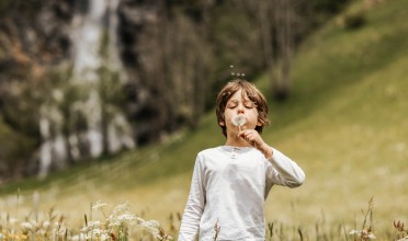 Kind auf der Wiese in der Natur mit einer Pusteblume