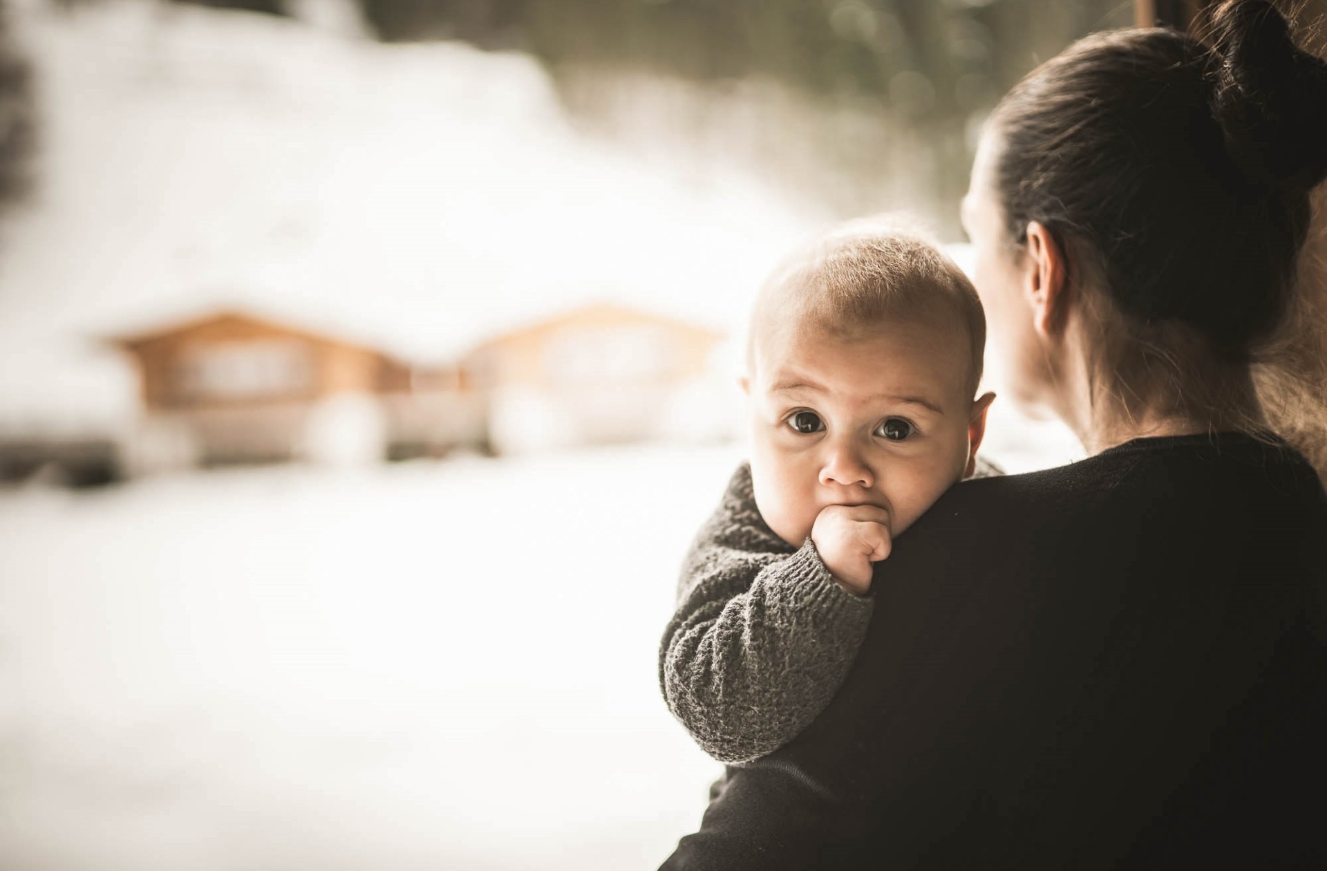 Il bambino è tenuto in braccio dalla madre e sta in piedi davanti alla finestra.