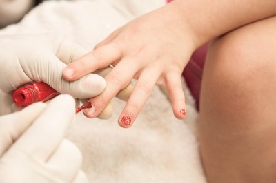 Una mano adulta applica lo smalto su un'unghia di un bambino
