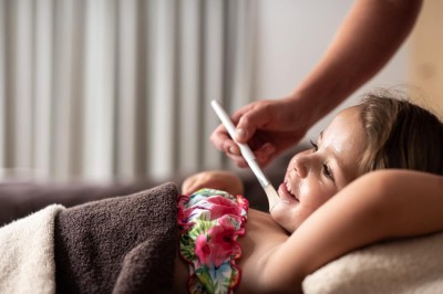 Una persona sdraiata con asciugamano riceve un trattamento viso con pennello