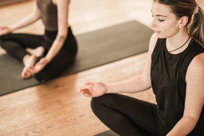 Donna che medita seduta su tappetino yoga con un'altra sullo sfondo