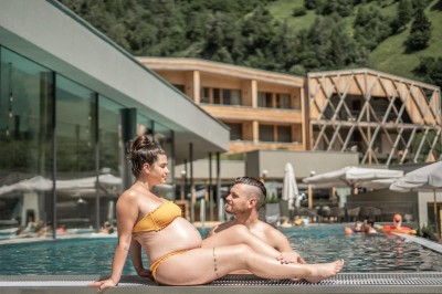 Donna incinta seduta a bordo piscina accanto a un uomo al resort