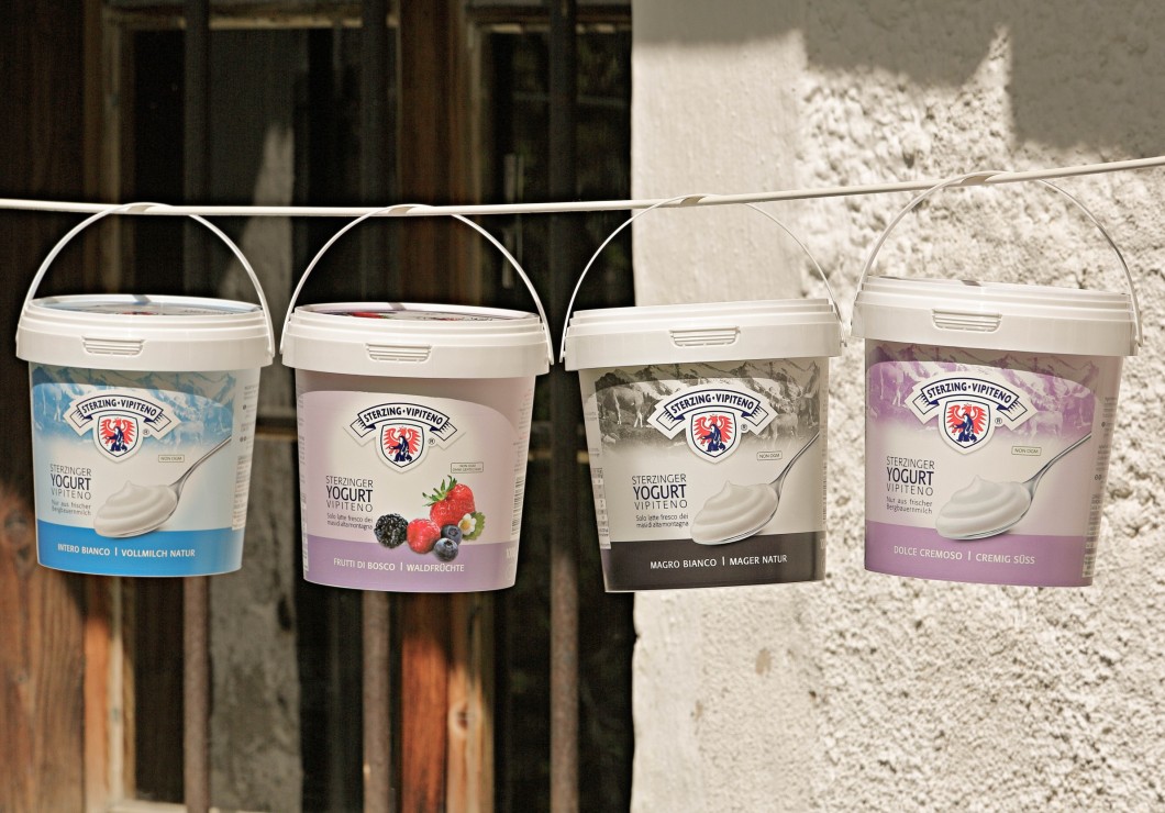 Tre secchi di latte e yogurt appesi a un filo davanti a un casolare di montagna.