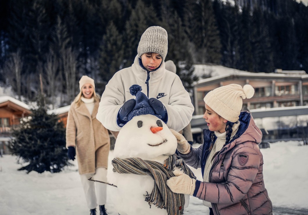Kinder bauen Schneemann mit einer Mütze und Schal