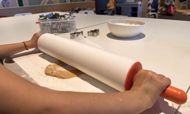 Mano che usa un mattarello per stendere l'impasto su un tavolo.