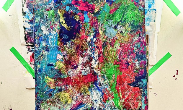 Un grande dipinto astratto appeso su un cavalletto con schizzi di colore