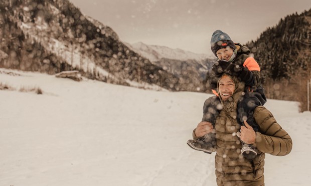 Kind sitzt auf den Schultern des Vaters mitten in der Schneelandschaft