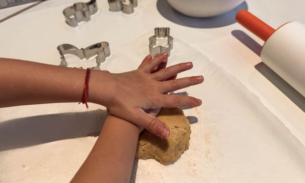 Mano di un bambino che preme l’impasto dei biscotti con formine.