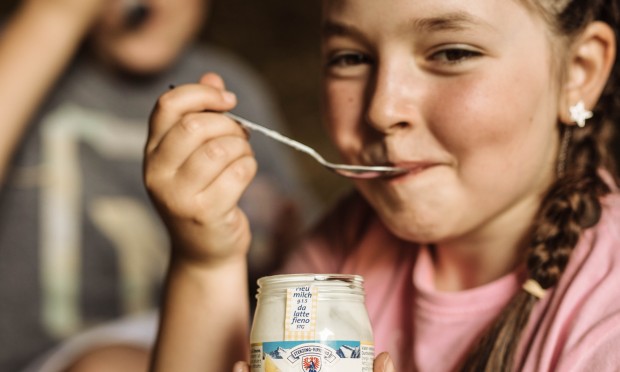 Una ragazza sorridente gusta uno yogurt bio con il cucchiaio e guarda felice.