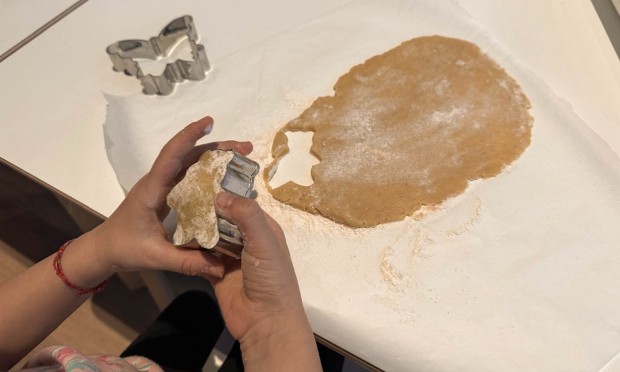 Mano che sagoma l’impasto per biscotti con formine su tavolo infarinato.