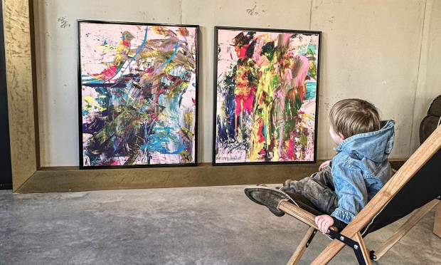 Ein Kind sitzt entspannt in einem Liegestuhl vor einer Wand mit abstrakten Gemälden.