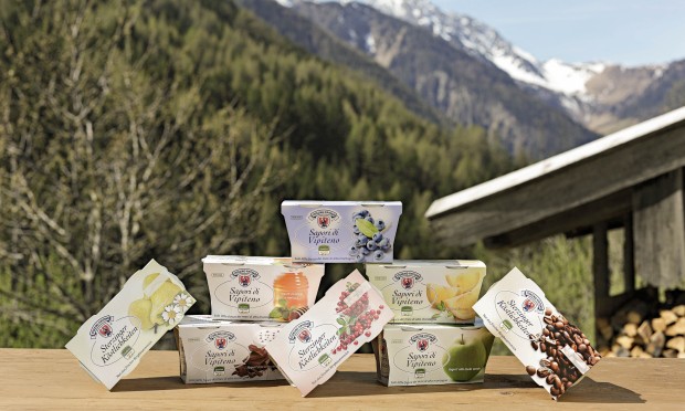 Prodotti lattiero-caseari di Vipiteno disposti su un tavolo di legno davanti alle montagne.