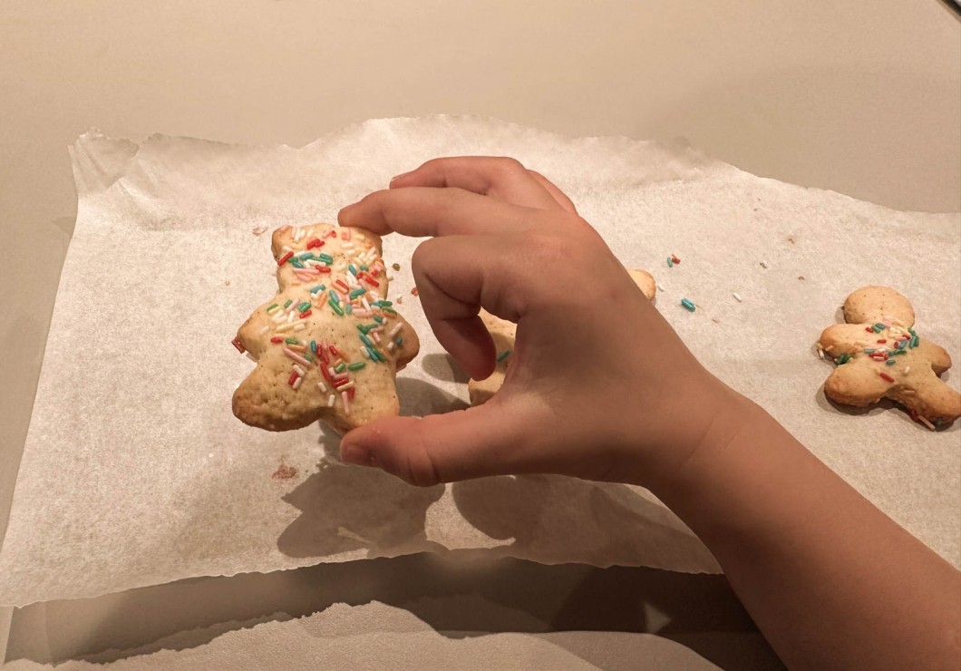 Una mano decora biscotti a forma di omino su carta da forno.