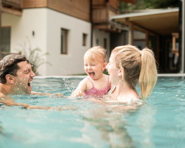 Un padre e una madre stanno giocando con la loro figlia in acqua in un hotel benessere per famiglie in Alto Adige.