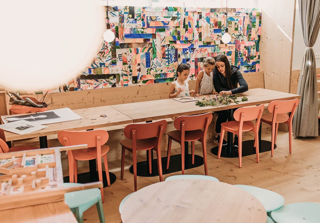 Ein kreativ gestalteter Raum mit bunten Zeichnungen an den Wänden und einer langen Tischreihe.