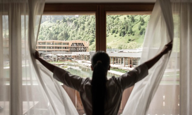 Dipendente apre le tende guardando verso il resort Feuerstein tra le montagne dalla camera.