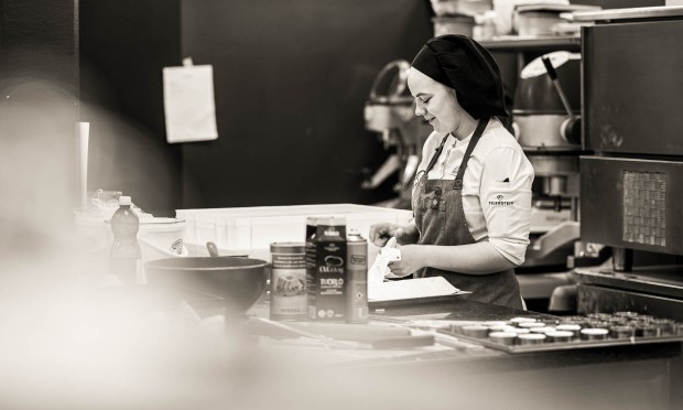 Cuoca del Feuerstein consulta un foglio mentre prepara ingredienti in cucina.