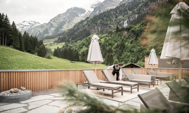 Terrazza panoramica del Feuerstein con sdraio e ombrelloni e vista sulle montagne, dipendente che sistema le sedie.