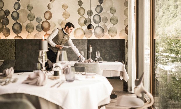 Cameriere del Feuerstein prepara i tavoli nel ristorante elegante con decorazioni artistiche alle pareti.