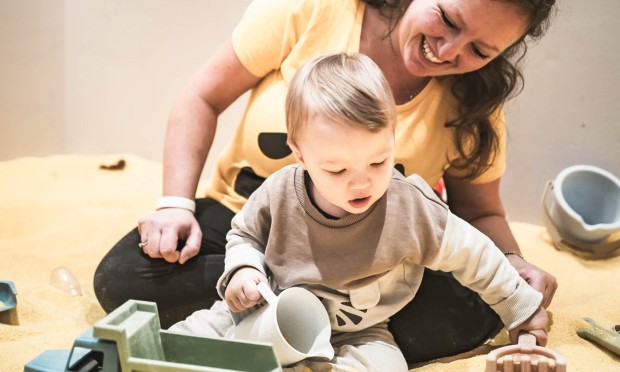 Mamma che gioca con il figlio nella sabbiera al Feuerstein, con camion giocattolo e secchiello.