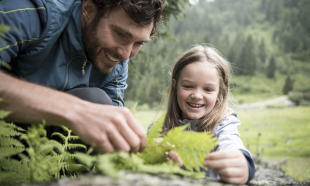 Vater hält zusammen mit Tochter ein Blatt in der Natur