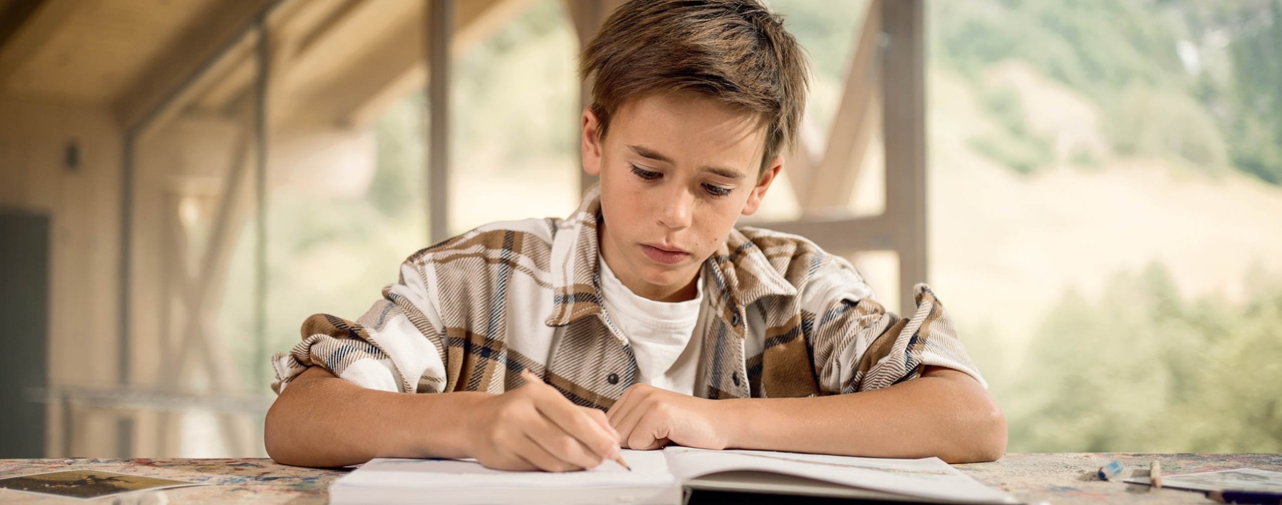 Bambino nel laboratorio del legno che sta scrivendo nel diario al Family Hotel Feuerstein in Alto Adige