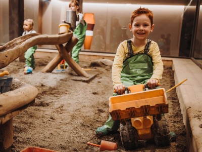 Junge sitzt auf Spielzeug Bagger im Matschraum