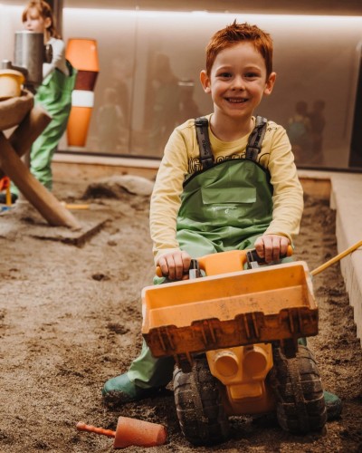 Ragazzo seduto su un escavatore giocattolo nella stanza del fango