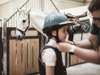 Reitlehrerin legt einem Kind einen Helm an