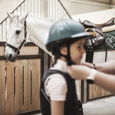 Un'istruttrice di equitazione mette il casco a un bambino